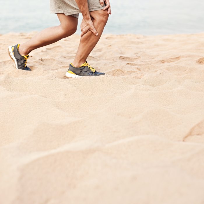 Muscle injury. Man with sprain thigh muscles. Athlete in sports shorts clutching his thigh muscles after pulling or straining them while jogging on the beach.