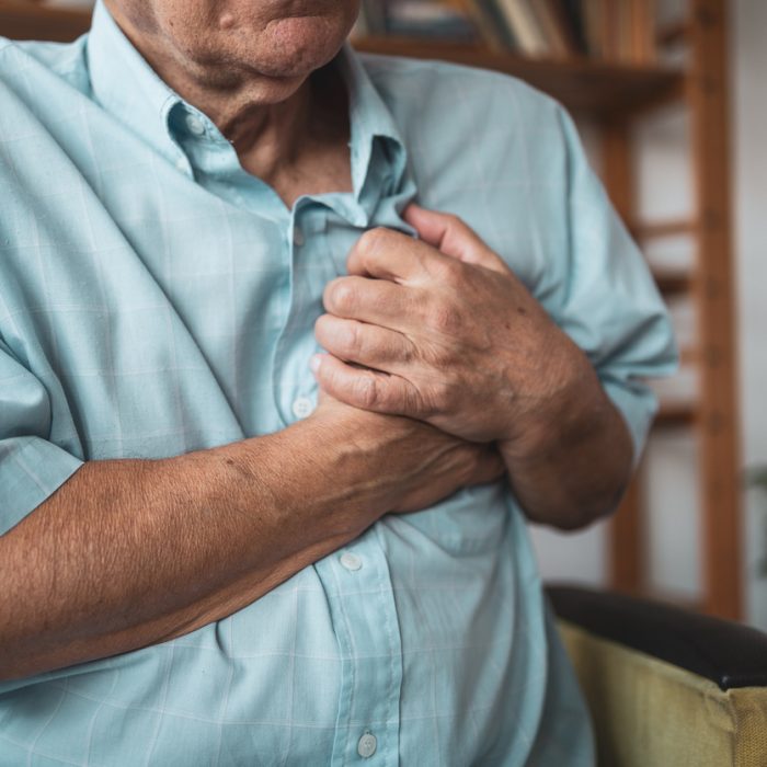 Close-up of an elderly man's hand held his chest in pain. Concept of heart disease.