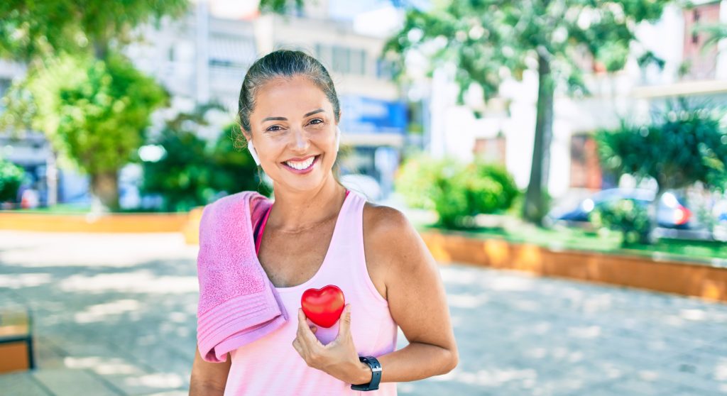 Middle age sportswoman asking for health care holding heart at the park