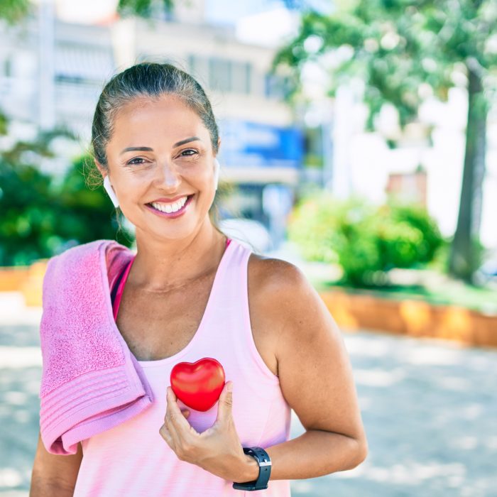 Middle age sportswoman asking for health care holding heart at the park
