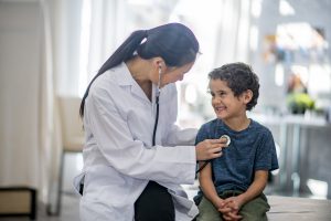 Boy smiling while the doctor checks his heart rate with a stethoscope.