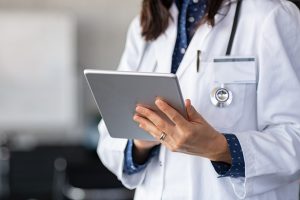 Closeup of female doctor in labcoat and stethoscope holding digital tablet, reading patient report.